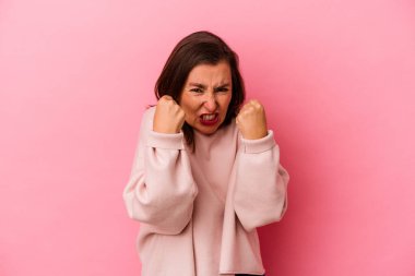 Pembe arka planda izole edilmiş orta yaşlı beyaz kadın yumruğunu kameraya gösteriyor, agresif yüz ifadesi var..