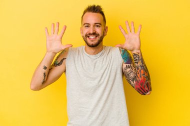 Sarı arka planda izole edilmiş genç dövmeli beyaz adam on numarayı elleriyle gösteriyor..