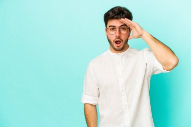 Mavi arka planda izole edilmiş genç beyaz adam yüksek sesle bağırıyor, gözleri açık ve elleri gergin tutuyor..