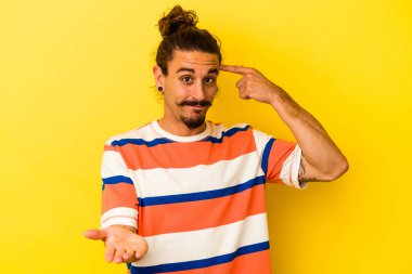 Sarı arka planda izole edilmiş uzun saçlı beyaz bir adam elinde bir ürün taşıyor..