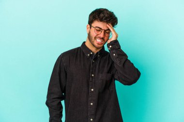 Kafkasyalı genç adam mavi arka planda izole edilmiş bir şekilde bir şeyi unutuyor. Alnına avuç içi ve gözlerini kapayarak vuruyor..