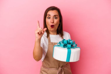 Orta yaşlı pasta şefi kadın mavi arka planda izole edilmiş bir pasta tutuyor. Bir fikri, ilham verici bir fikri var..