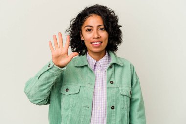Beyaz arka planda izole edilmiş genç kıvırcık Latin kadın gülümseyerek beş numarayı parmaklarıyla gösteriyor..