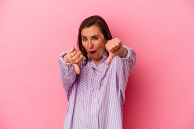 Pembe arka planda soyutlanmış orta yaşlı beyaz kadın baş parmağını aşağı gösteriyor ve hoşlanmadığını ifade ediyor..