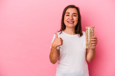 Orta yaşlı, elinde nohut kavanozu olan beyaz bir adam pembe arka planda izole edilmiş gülümsüyor ve başparmağını kaldırıyor.