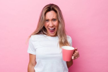 Pembe arka planda izole edilmiş pembe kupa tutan genç Avustralyalı kadın çok sinirli ve agresif çığlıklar atıyor..