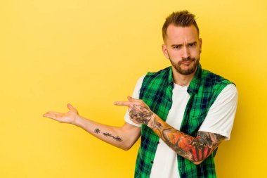 Sarı arka planda izole edilmiş genç, dövmeli beyaz bir adam..