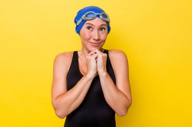 Sarı arka planda izole edilmiş genç Avustralyalı yüzücü kadın ellerini çenesinin altında tutuyor, mutlu bir şekilde yana bakıyor..