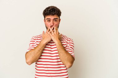 Beyaz arka planda izole edilmiş genç beyaz adam şok olmuş, ağzı ellerle kaplanmış, yeni bir şey keşfetmeye hevesli..