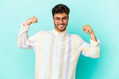 Mavi arka planda izole edilmiş genç beyaz adam güçlü bir hareket sergiliyor kollarıyla, kadınsı gücün sembolü.