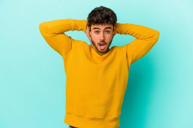 Genç beyaz adam mavi arka planda izole edilmiş bağırıyor, çok heyecanlı, tutkulu, bir şeyden memnun..