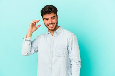 Mavi arka planda izole edilmiş genç beyaz bir adam bir şeye gülüyor, ağızlarını ellerle kapatıyor..