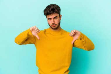 Mavi arka planda izole edilmiş genç beyaz bir adam hoşlanmadığı bir jest yapıyor. Anlaşmazlık konsepti.