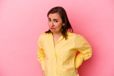 Pembe arka planda soyutlanmış orta yaşlı beyaz kadın kafası karışmış, şüpheli ve kendinden emin değil..