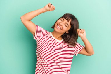 Genç melez kadın mavi üzerine izole edilmiş özel bir günü kutluyor, atlıyor ve enerji ile kollarını kaldırıyor..