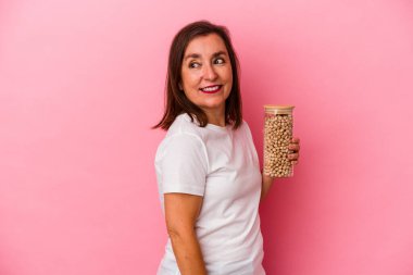 Orta yaşlı beyaz bir adam pembe arka planda izole edilmiş nohut kavanozunu tutuyor. Gülümsüyor, neşeli ve keyifli görünüyor..