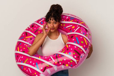 Beyaz arka planda izole edilmiş şişme bir donut tutan genç bir ırk kadını ve dudaklarında bir sır saklayan parmaklar..