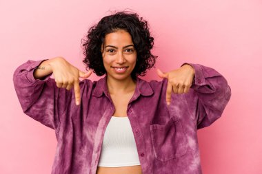Pembe arka planda izole edilmiş genç kıvırcık Latin kadın parmakları aşağıda, pozitif duygu..