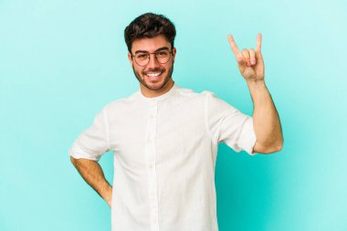 Mavi arka planda izole edilmiş genç beyaz adam boynuzlarını devrim konsepti olarak gösteriyor..