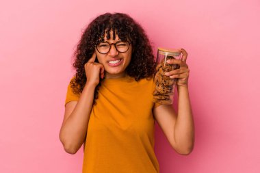 Elinde kurabiye kavanozu tutan genç bir ırk kadını pembe arka planda izole edilmiş kulakları elleriyle kapatıyor..