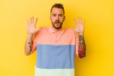 Sarı arka planda izole edilmiş genç dövmeli beyaz adam gökyüzüne haykırıyor, bakıyor, hayal kırıklığına uğruyor..