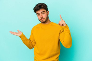 Kafkasyalı genç adam mavi arka planda izole edilmiş ve elinde bir ürün tutuyor..