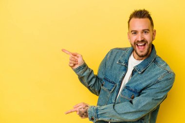 Sarı arka planda izole edilmiş genç, dövmeli beyaz adam işaret parmağıyla işaret ederek heyecanlanıyor..