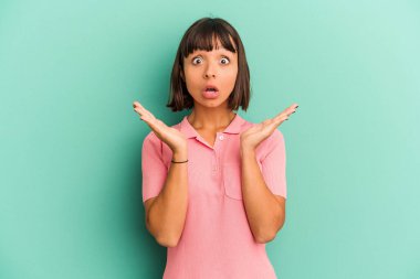 Genç melez kadın mavi üzerine izole edilmiş şaşırmış ve şok olmuş..