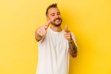 Sarı arka planda izole edilmiş genç, dövmeli beyaz adam. Önü işaret eden neşeli gülümsemeler..