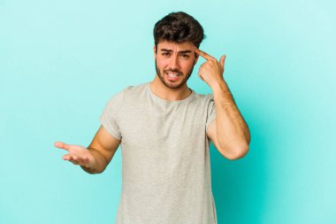 Mavi arka planda izole edilmiş genç beyaz adam işaret parmağıyla bir hayal kırıklığı jesti gösteriyor..