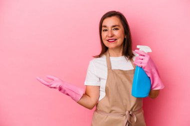 Orta yaşlı, beyaz bir kadın evini temizliyor. Pembe arka planda izole edilmiş. Bir avuç içinde fotokopi alanı var..