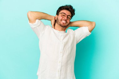 Kafkasyalı genç adam mavi arka planda izole edilmiş. Kendine güveniyor, elleri başının arkasında..