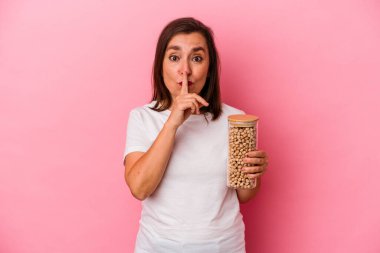 Orta yaşlı beyaz bir adam pembe arka planda izole edilmiş nohut kavanozunu tutuyor ya sır saklıyor ya da sessizlik istiyor..