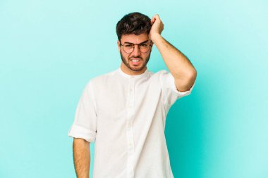 Kafkasyalı genç adam mavi arka planda izole edilmiş bir şekilde bir şeyi unutuyor. Alnına avuç içi ve gözlerini kapayarak vuruyor..