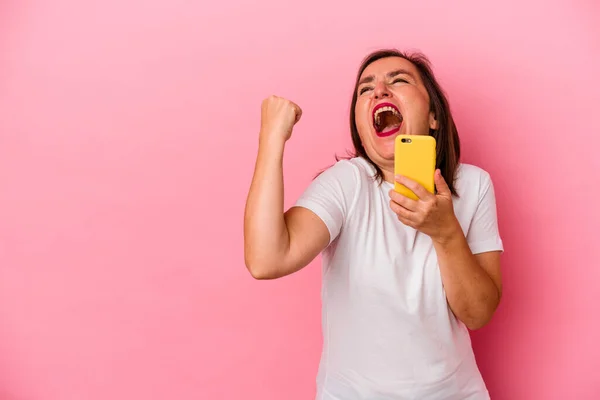 中年妇女手持手机 手持粉色背景孤零零的中年妇女获胜后举起拳头 获胜者的概念 — 图库照片