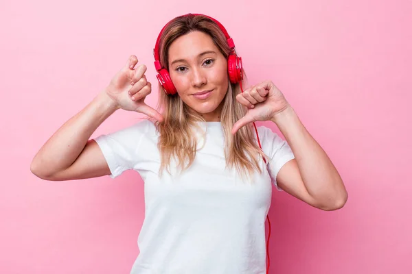 ピンクの背景に隔離された音楽を聴いている若いオーストラリアの女性は誇りと自信を感じています 次の例に従うこと — ストック写真