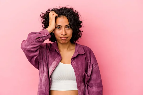 Young curly latin woman isolated on pink background forgetting something, slapping forehead with palm and closing eyes.