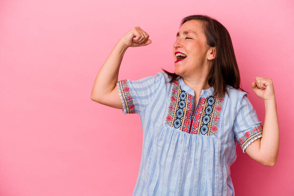 Кавказская женщина средних лет изолирована на розовом фоне, поднимая кулак после победы, концепция победителя.