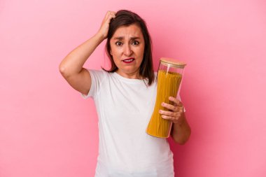 Orta yaşlı, elinde makarna kavanozu olan beyaz bir kadın pembe arka planda izole edilmiş şok geçiriyordu. Önemli bir toplantıyı hatırladı..