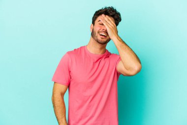 Mavi arka planda izole edilmiş genç beyaz adam ellerini başının üstünde tutarak neşe içinde gülüyor. Mutluluk kavramı.