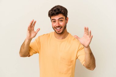 Beyaz arka planda izole genç beyaz adam hoş bir sürpriz alıyor, heyecanlı ve el kaldırıyor..