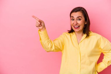 Pembe arka planda izole edilmiş orta yaşlı beyaz kadın işaret parmağıyla işaret ederek gülümsüyor..