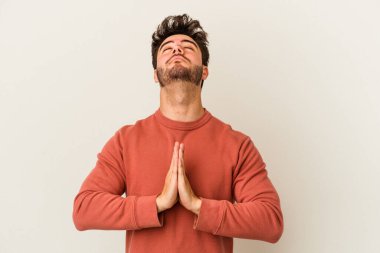 Beyaz arka planda izole edilmiş genç beyaz bir adam el ele tutuşup, ağız kenarında dua ediyor, kendinden emin..