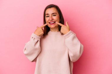 Orta yaşlı beyaz kadın pembe arka planda izole edilmiş gülücükler içinde, parmaklarını ağıza doğrultuyor..