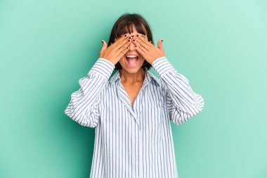 Mavi üzerine izole edilmiş genç bir ırk kadını elleriyle gözlerini kapatıyor, geniş bir gülümsemeyle bir sürpriz bekliyor..