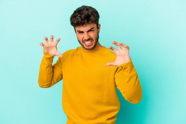 Mavi arka planda izole edilmiş genç beyaz adam pençelerini kedi taklidi yaparken gösteriyor, agresif bir hareket..