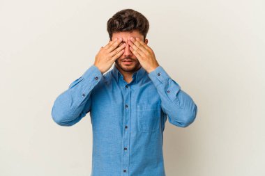 Beyaz arka planda izole edilmiş genç beyaz bir adam elleriyle gözlerini kapatmaktan korkuyor..