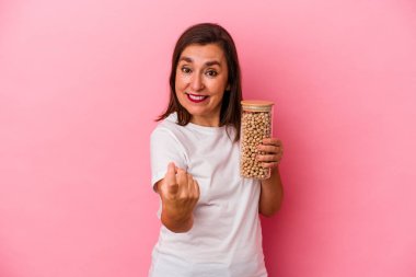 Orta yaşlı beyaz bir adam pembe arka planda izole edilmiş nohut kavanozunu tutarken seni işaret ediyor sanki davet ediyormuş gibi..