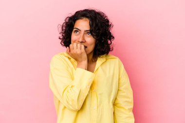 Genç kıvırcık Latin kadın pembe arka planda izole olmuş tırnak yiyor, gergin ve çok endişeli..