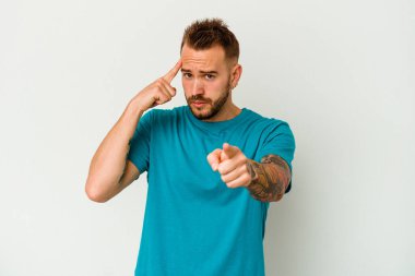 Beyaz arka planda izole edilmiş genç dövmeli beyaz adam şakağı işaret ediyor, düşünüyor ve bir göreve odaklanıyor..